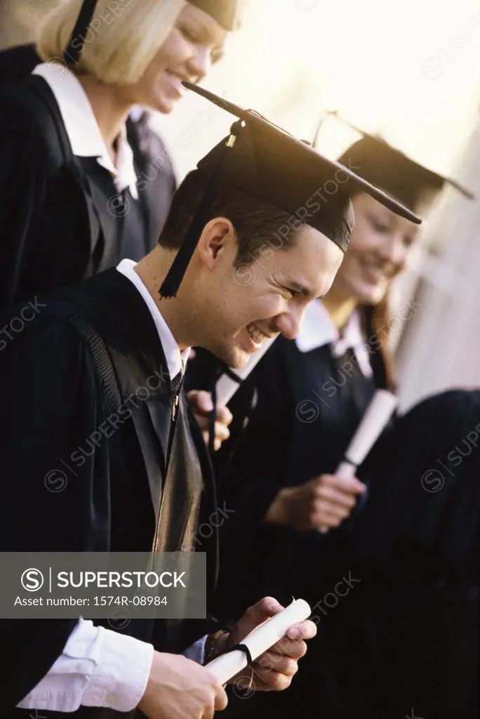 Side profile of young graduates holding diplomas smiling