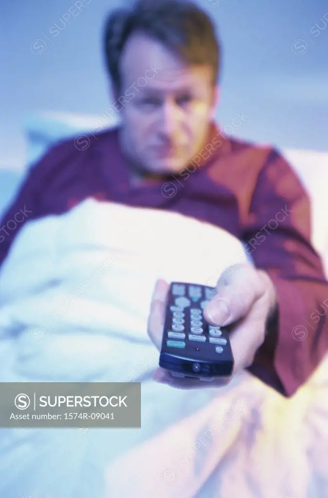 Portrait of a mid adult man lying in bed holding a remote control