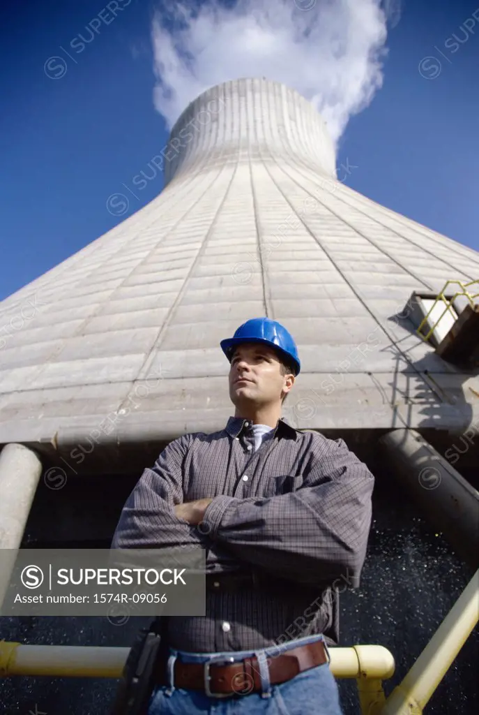 Low angle view of a worker standing beside a smoke stack at a power plant