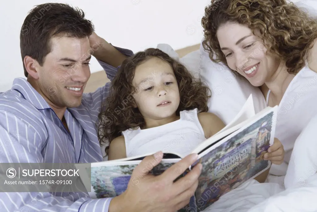 Parents and their daughter lying in bed together reading a book