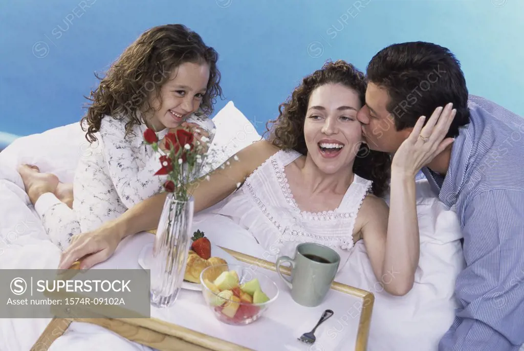 Parents and their daughter in bed with a breakfast tray