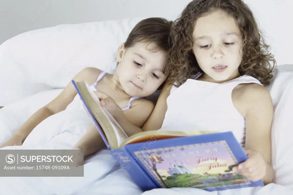 Two sisters lying in bed together reading a book