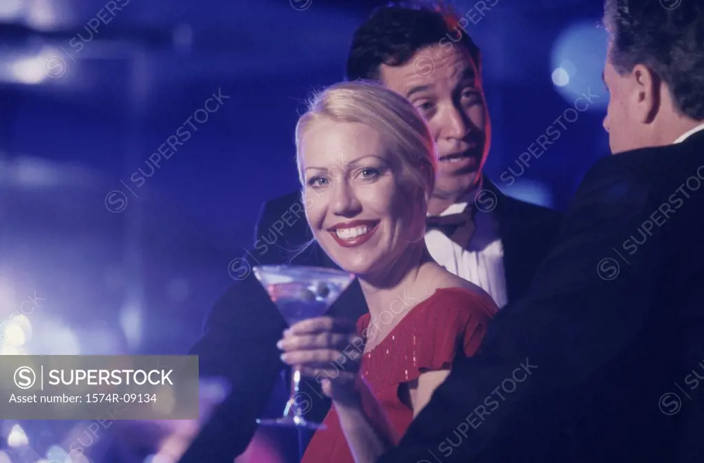 Woman holding a martini glass standing with two men at a bar