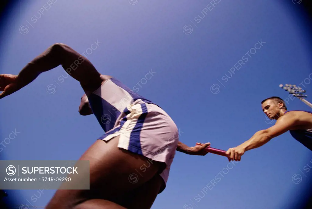 Low angle view of two male athletes passing a relay baton