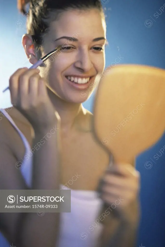 Young woman applying make-up in front of a mirror