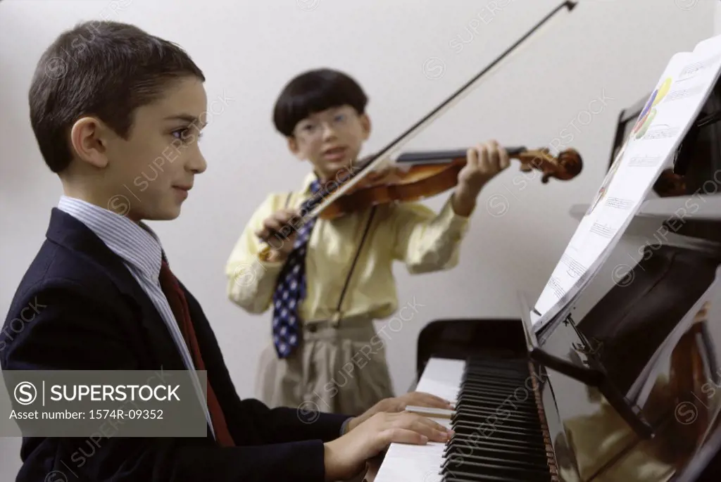 Boy playing the piano and another playing the violin