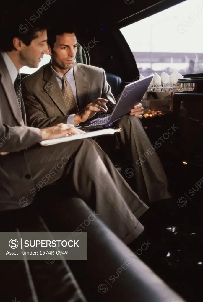 Two businessmen using a laptop in a car