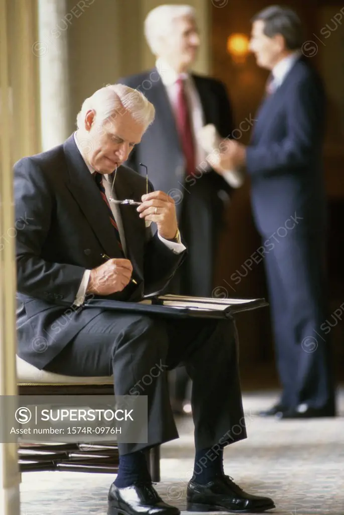 Businessman writing in a file with two businessmen standing behind him