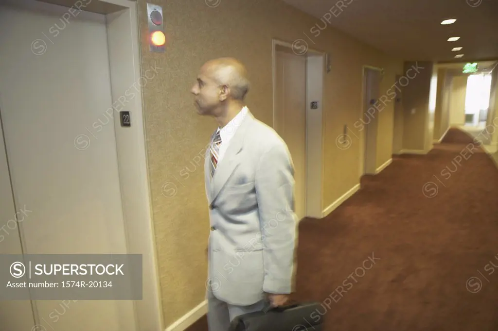 Side profile of a businessman holding his bag and standing in front of an elevator