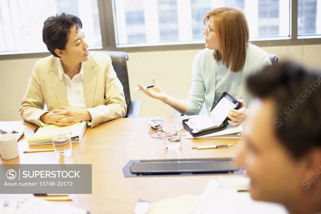Two businesswomen and a businessman talking in a conference room