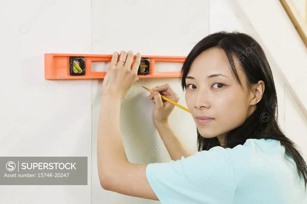 Portrait of a young woman using spirit level to mark on a wall