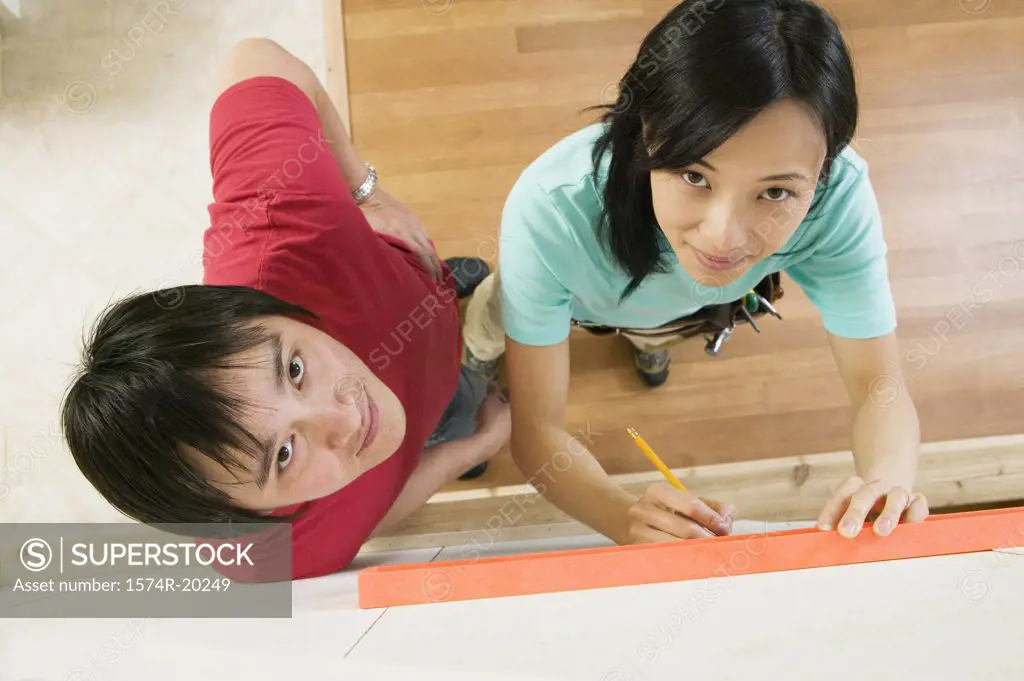 High angle view of a young woman using a spirit level to mark on a wall with a young man standing beside her