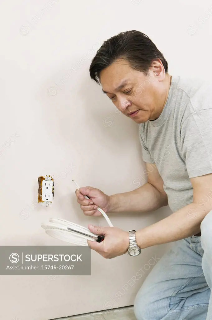 Side profile of a mid adult man holding wire and a screwdriver near a power outlet