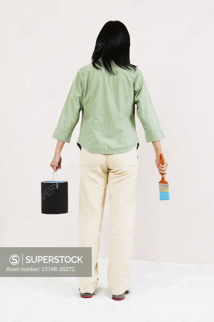 Rear view of a woman holding a paint can and a paintbrush