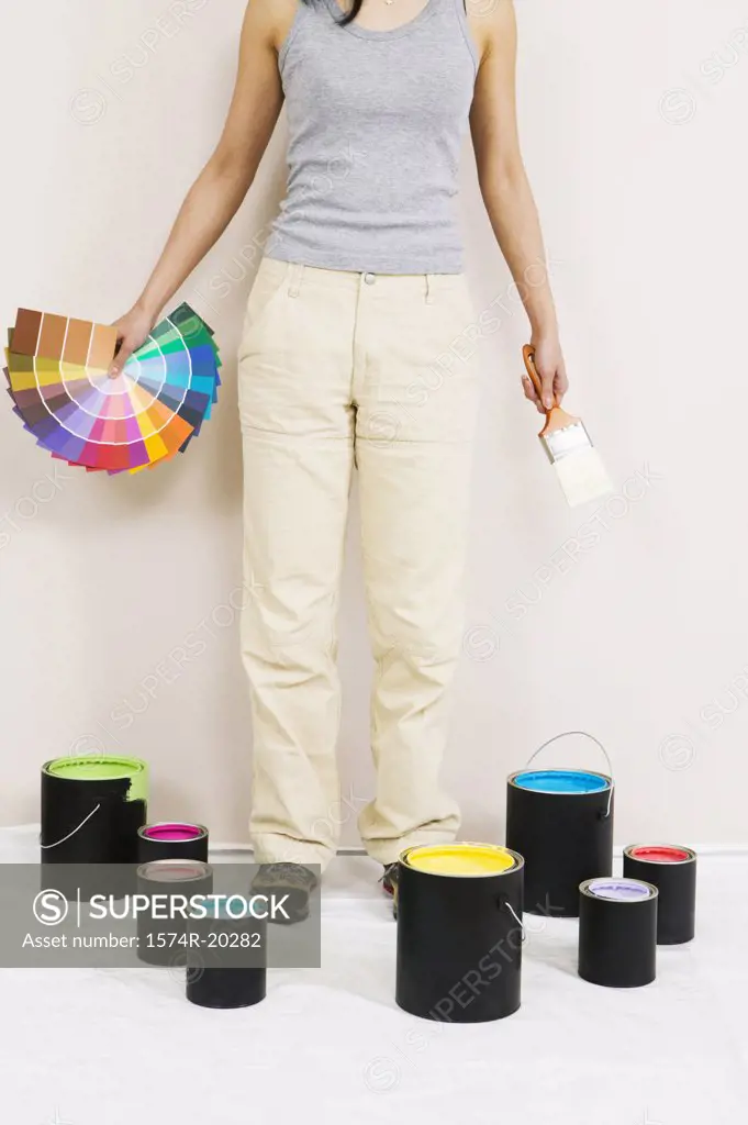 Low section view of a young woman holding color swatches and a paintbrush