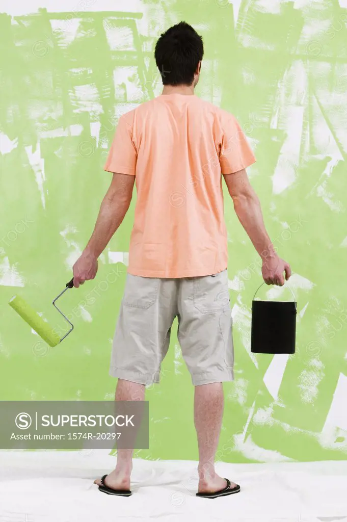 Rear view of a young man holding a paint can and a paint roller