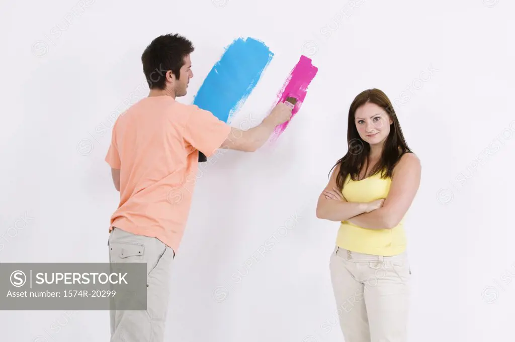 Young man painting a wall with a young woman standing beside him
