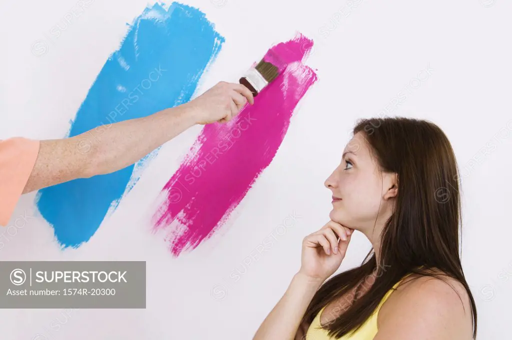 Side profile of a young woman looking at a person's hand painting a wall