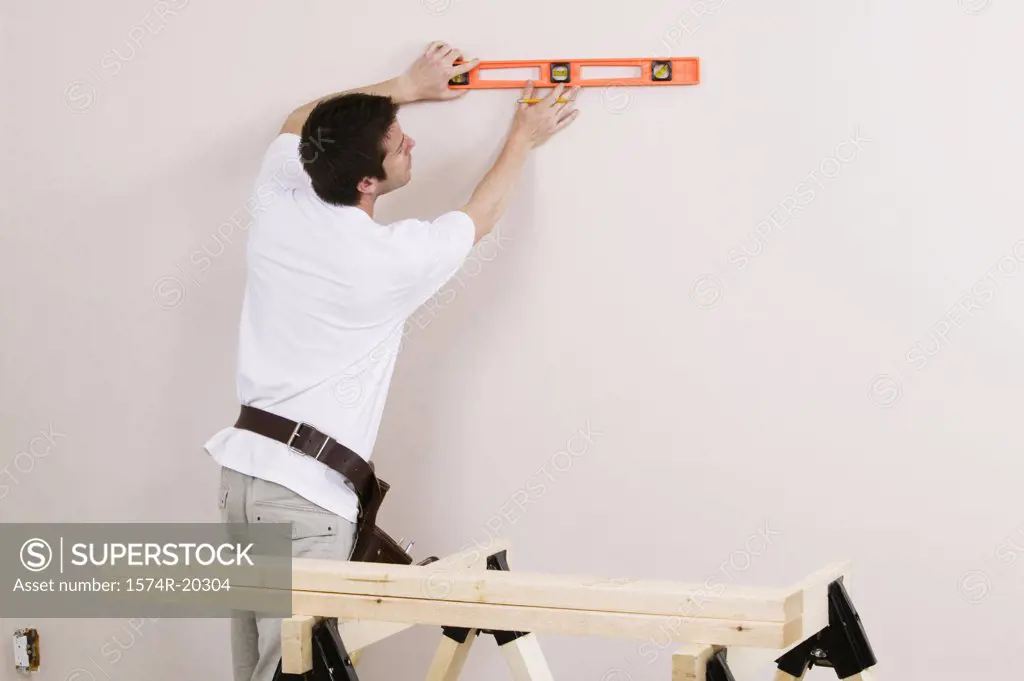 Rear view of a young man using a spirit level to mark on a wall