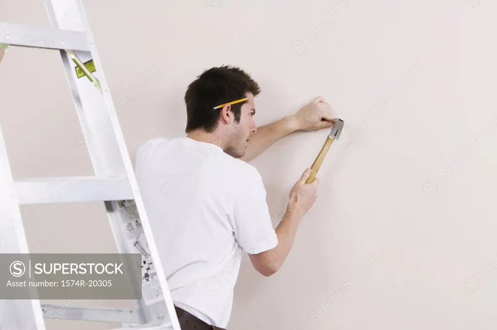 Rear view of a young man hammering a nail into a wall