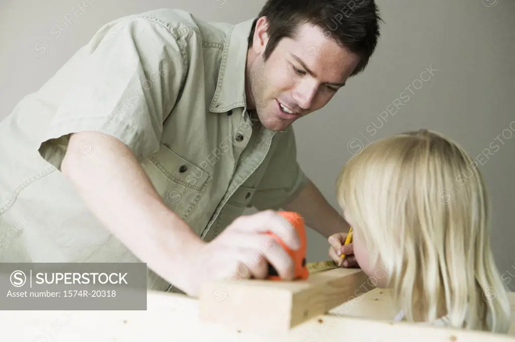 Father holding a tape measure with his daughter marking on a plank with a pencil
