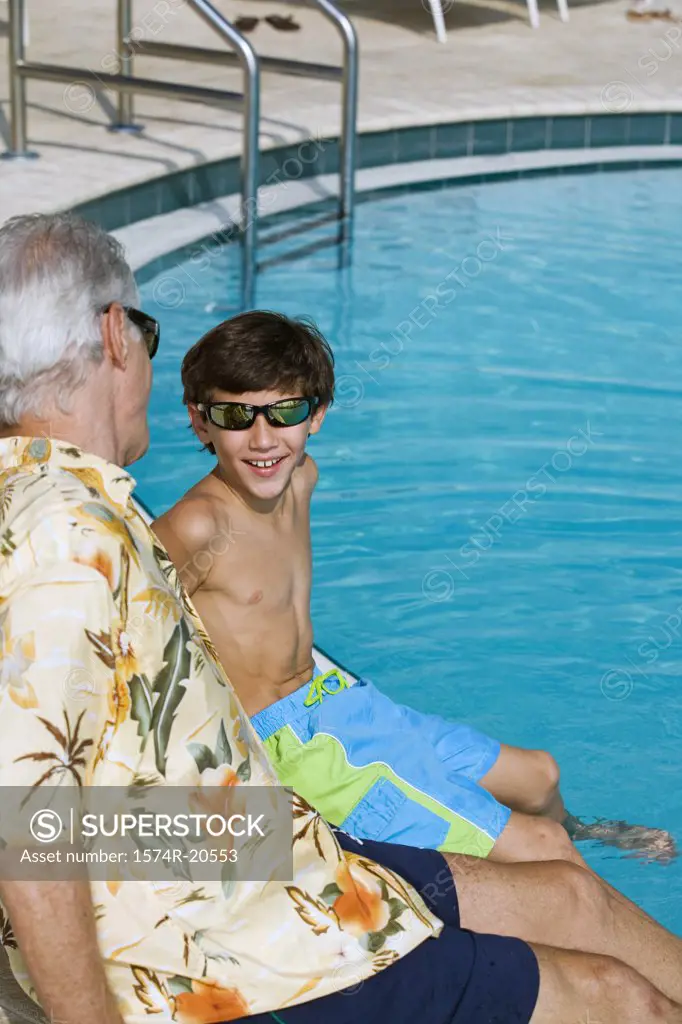 Side profile of a senior man sitting with his grandson at poolside