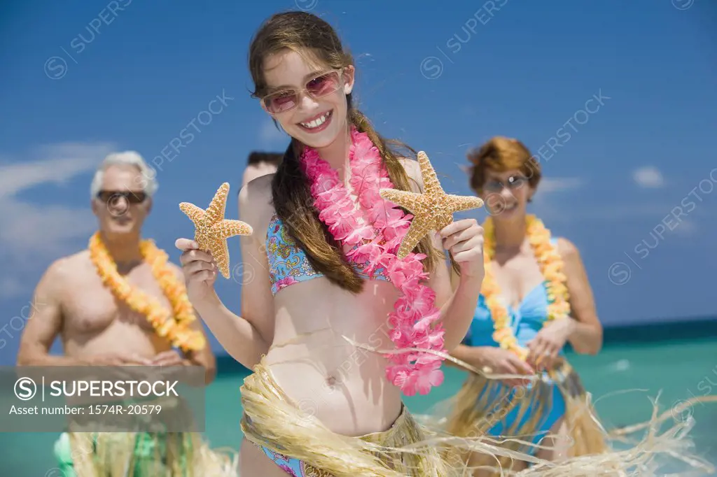 Close-up of a girl holding two starfish with her grandparents standing behind her on the beach