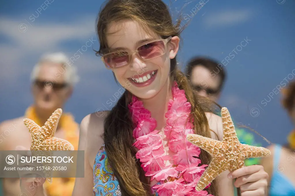 Close-up of a girl holding two starfish with her grandparents and father in the background