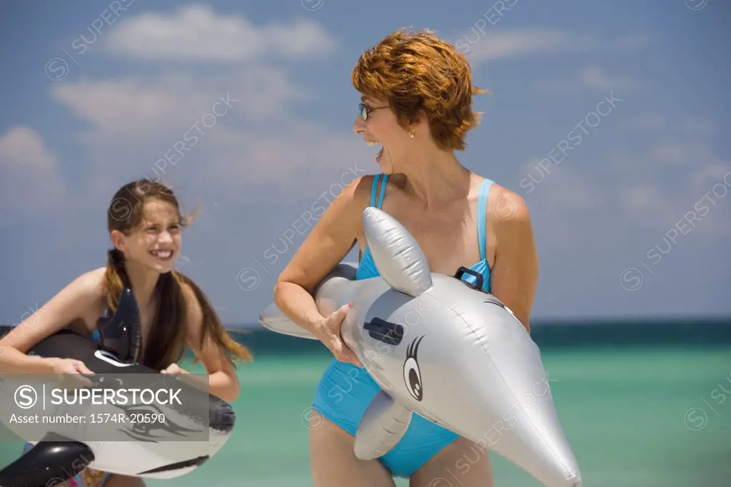 Senior woman playing with her granddaughter holding fish shaped floats on the beach
