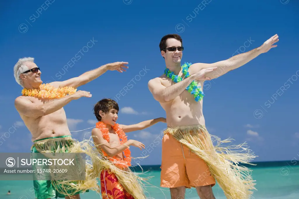 Boy hula dancing with his grandfather and father on the beach