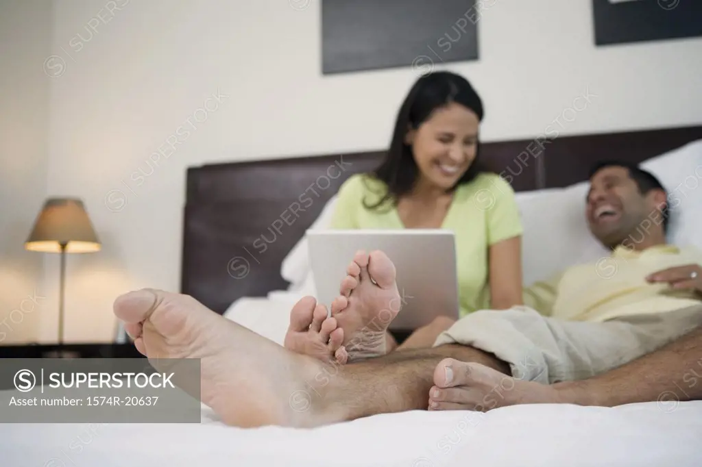 Mature man lying in the bed with a mature woman sitting beside him with a laptop on her lap
