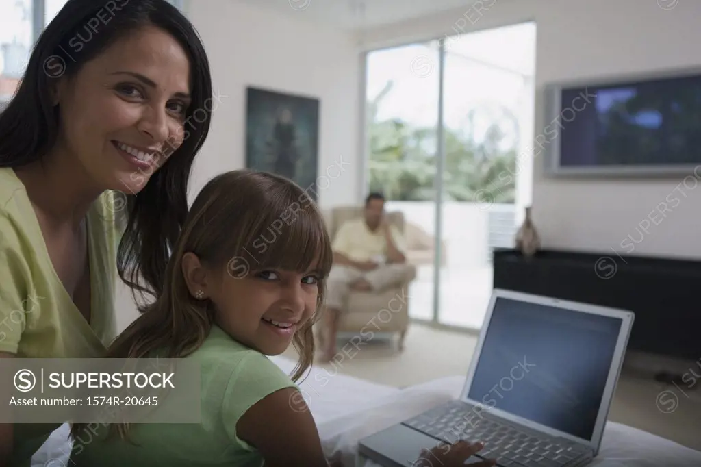 Portrait of a girl using a laptop with her mother sitting behind her