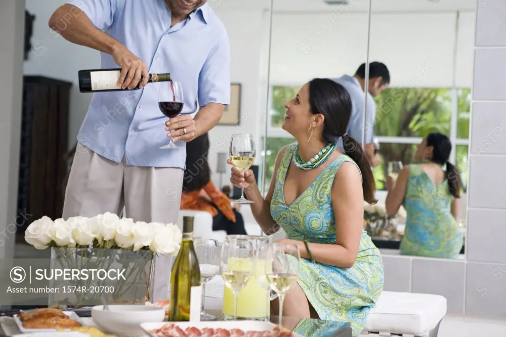 Mature man pouring red wine into a wineglass and a mature woman looking at him