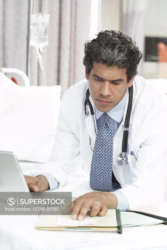 Close-up of a male doctor using a laptop while reading a document