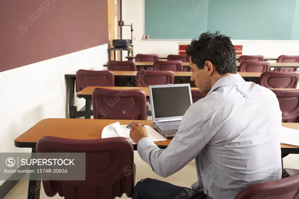 Rear view of a college student sitting in a lecture hall in front of a laptop