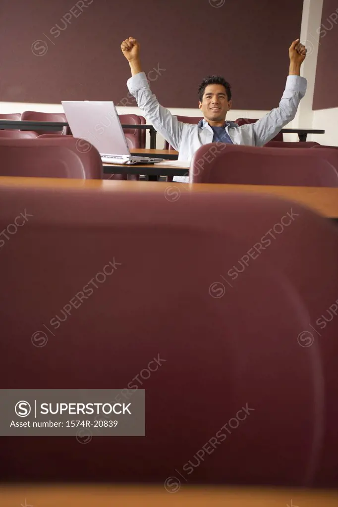 College student sitting in a lecture hall with his arms raised