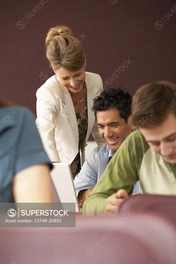 Professor looking at a laptop of a college student in a lecture hall and smiling