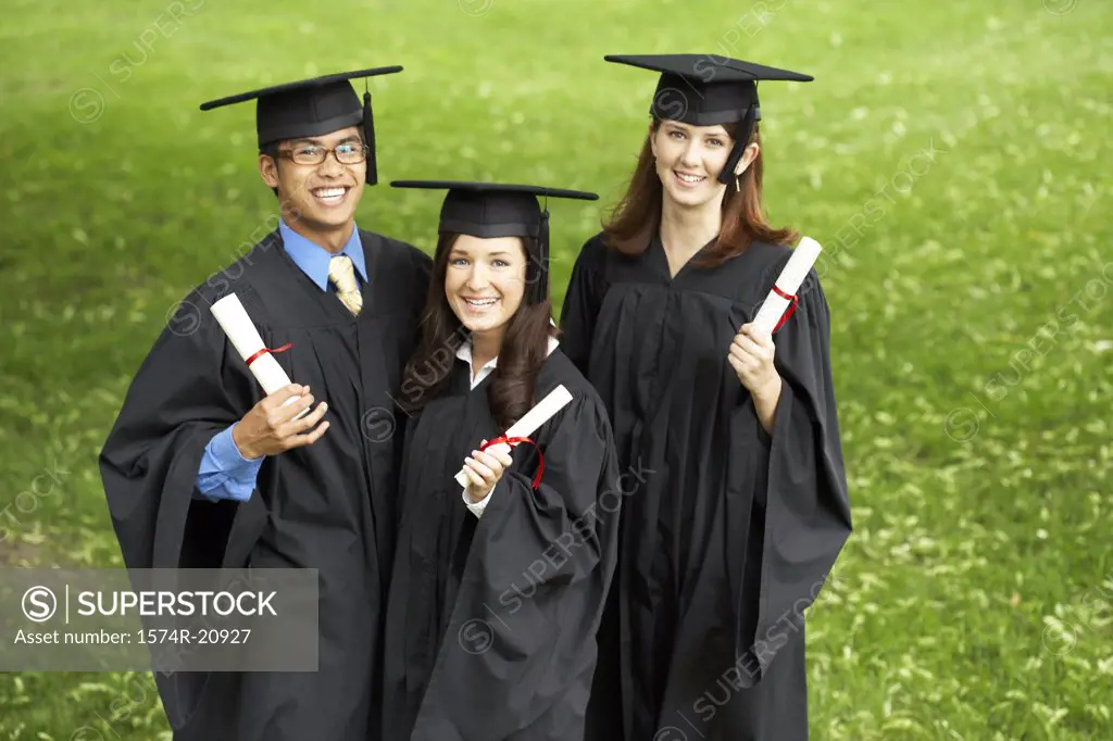 Two female graduates and a male graduate holding diplomas