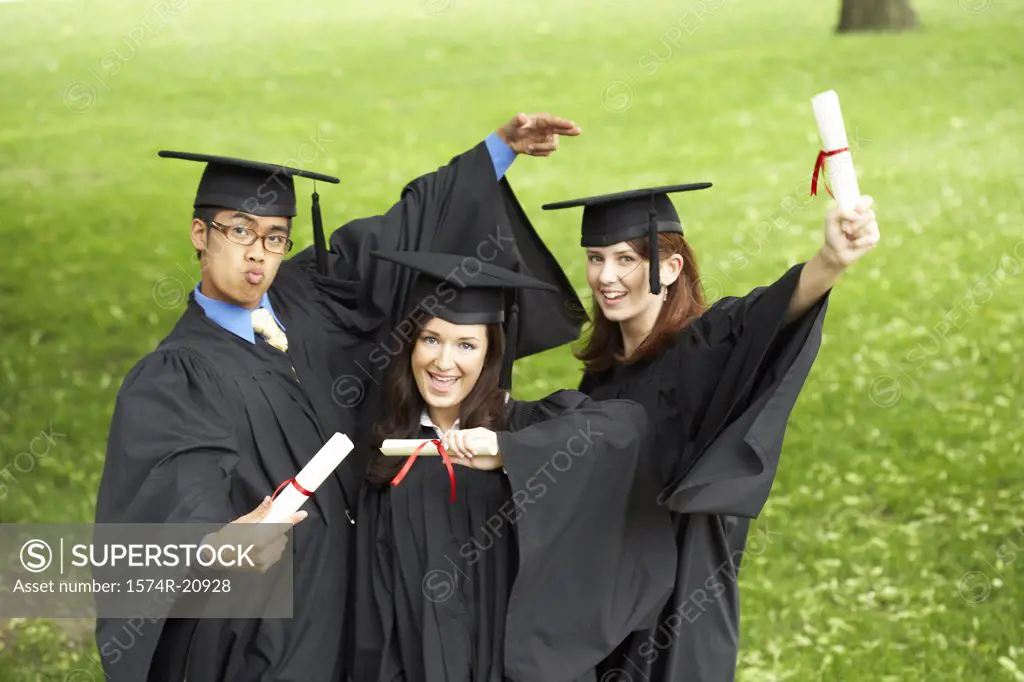 Two female graduates and a male graduate holding diplomas