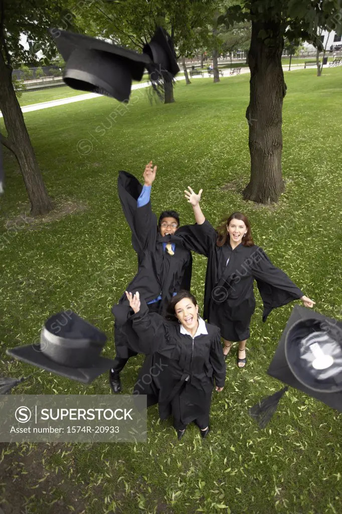 Two female graduates and a male graduate throwing their mortarboards in the air