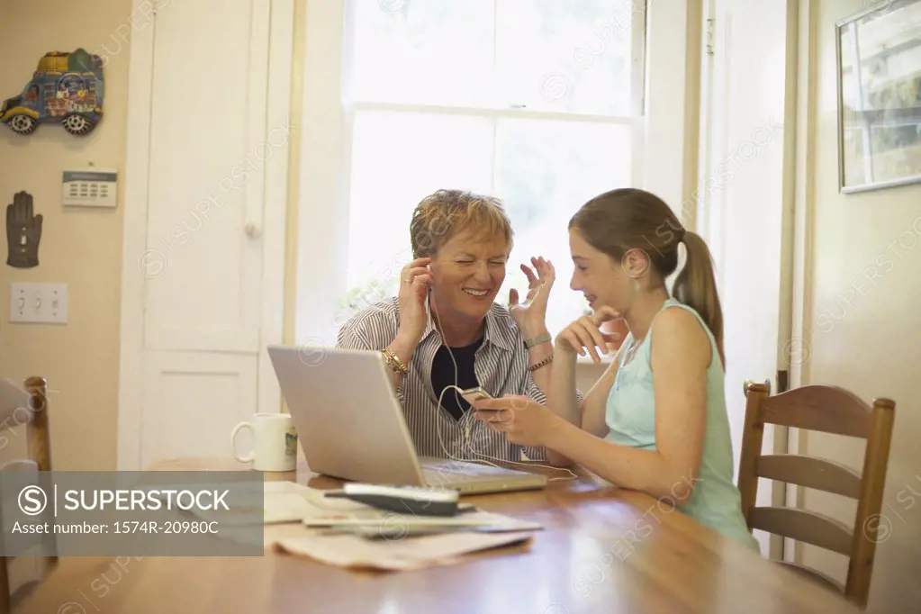 Mature woman wearing headphones and listening to music with her granddaughter sitting beside her