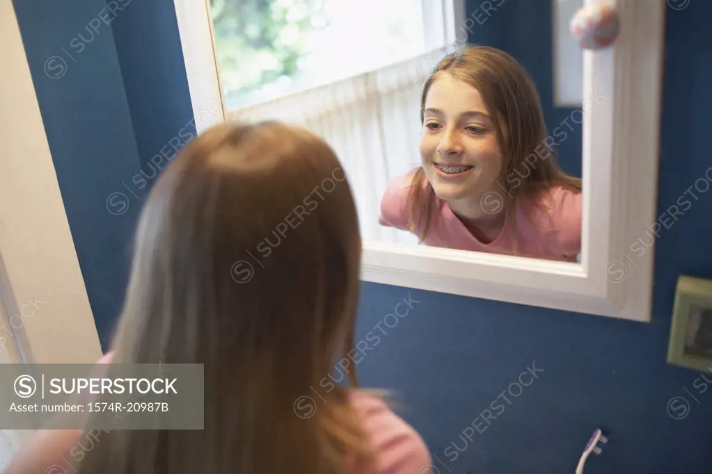 Reflection of a teenage girl looking at her teeth in a mirror