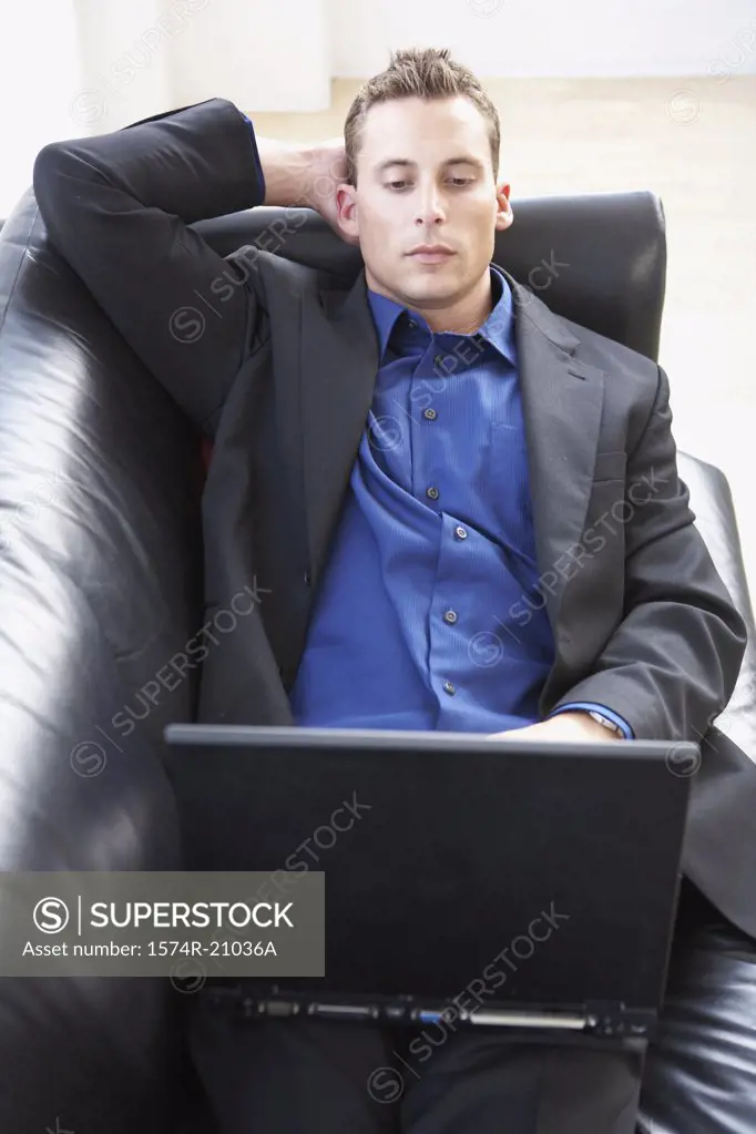 High angle view of a businessman reclining on a couch and using a laptop