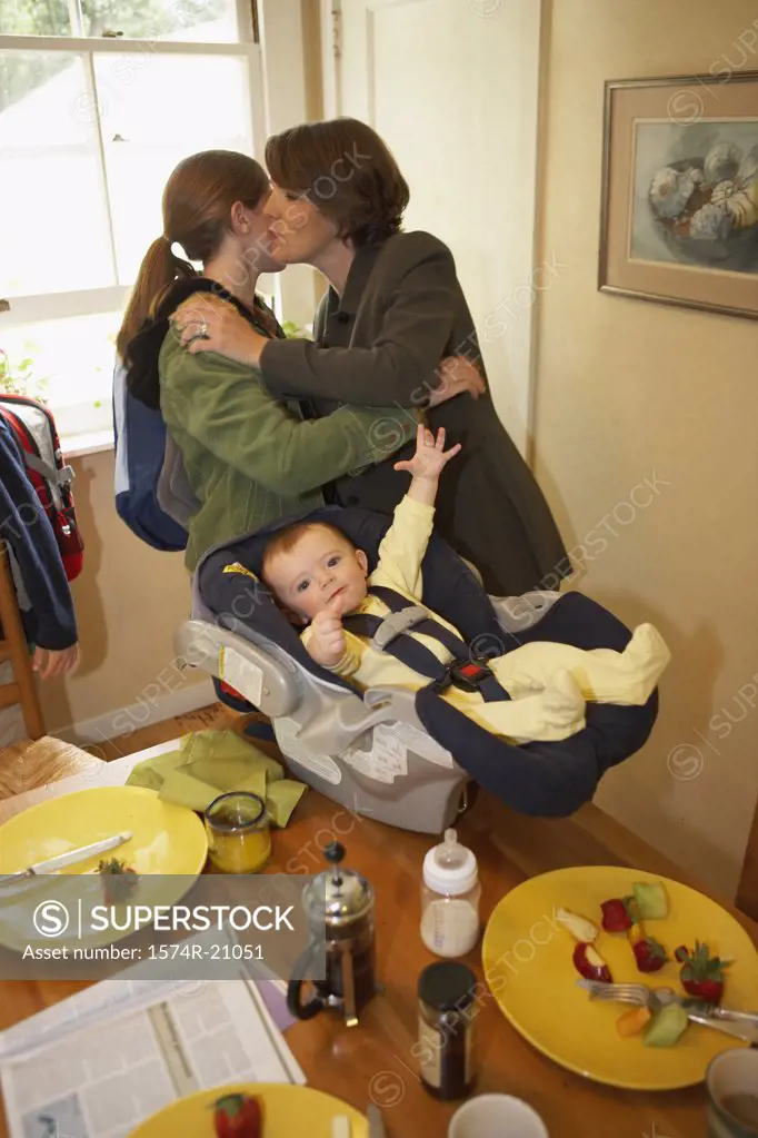 Side profile of a mid adult woman kissing her daughter with her son in a baby seat beside them