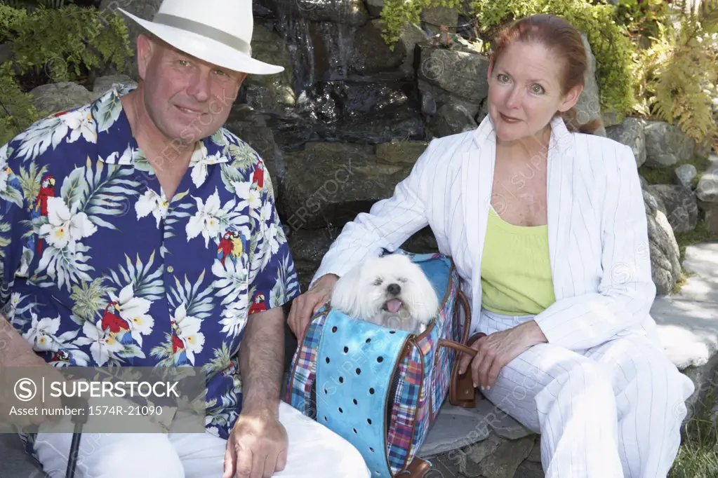 Close-up of a mature couple sitting in a garden with a dog in a bag