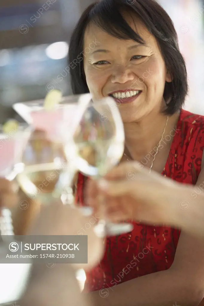 Human hands toasting with glasses and a mature woman smiling in the background