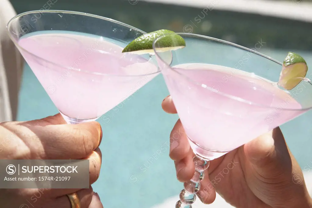 Close-up of two people's hands toasting with martini glasses