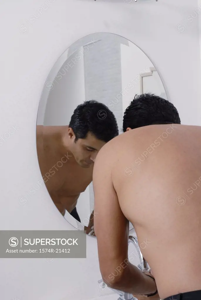 Rear view of a mid adult man washing his face in front of a mirror in the bathroom
