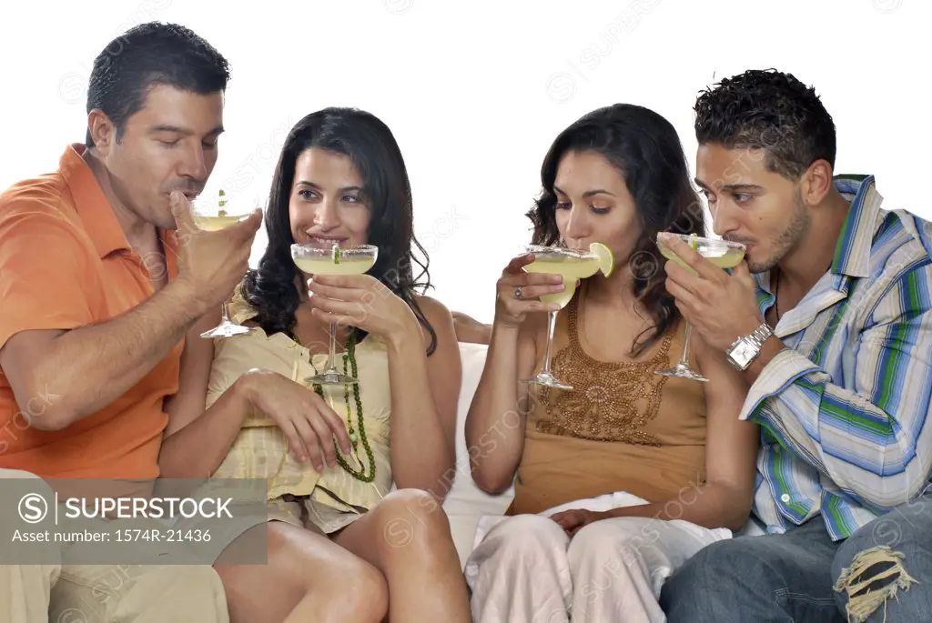 Mid adult couple and a young couple sitting on a couch and drinking margaritas
