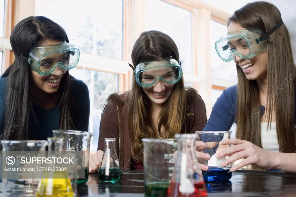 Three students with beakers laughing in a science lab